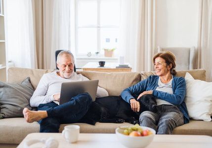 smiling senior couple on couch with dog and computer reviewing Medicare options