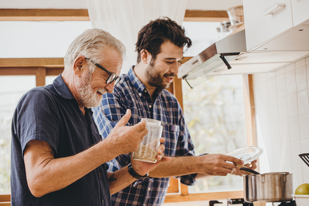 a smiling father and son cooking in a bright kitchen with big windows.