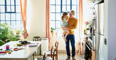 dad holding young daughter in bright kitchen while she drinks from a cup