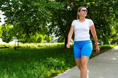 A middle-aged woman in athletic clothing walks on the sidewalk