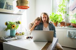 man and woman sitting close at kitchen table looking at laptop