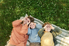 Mom and two young children lay in the grass and look up at the sky