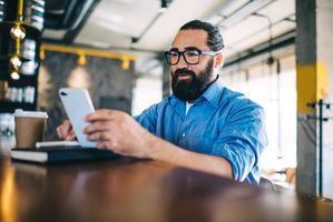 bearded man in coffeeshop using smartphone to work