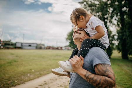 Father walking in the park with his daughter on his shoulders