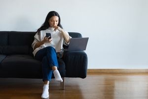 Woman on her phone and laptop on a couch
