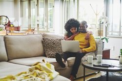 Young man and woman sitting on couch at home reviewing information on laptop.