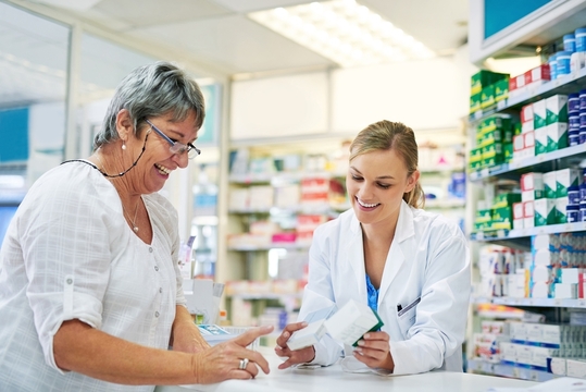 a woman and pharmacist discussing a prescription at the pharmacy counter.