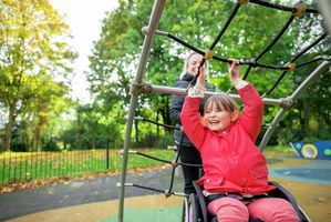 Girl using wheelchair playing on jungle gym with mother