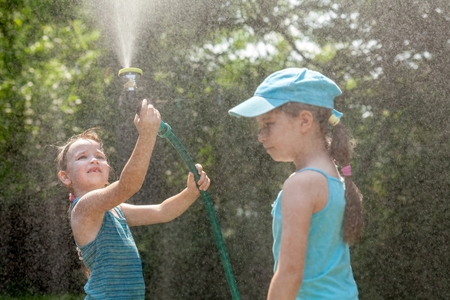 two elementary school aged children play with the garden hose