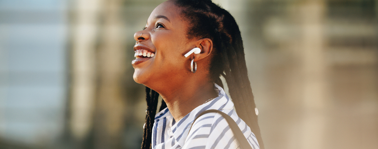 smiling woman wearing ear buds standing outside on city street