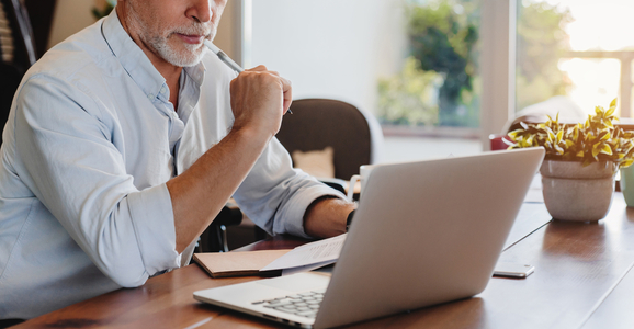 Senior man looking at laptop and papers