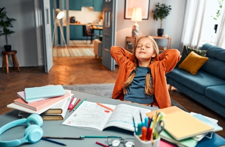 grade school-aged girl leans back in chair, takes relaxing study break at her living room desk