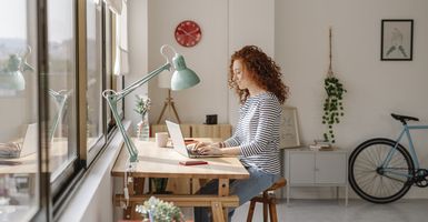 Young woman with curly hair working on her laptop in a modern apartment 