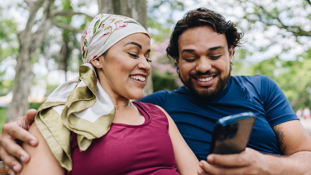 Happy couple looks at their phone together while sitting on a bench in the park