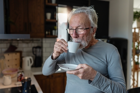 an older man sips coffee in his kitchen