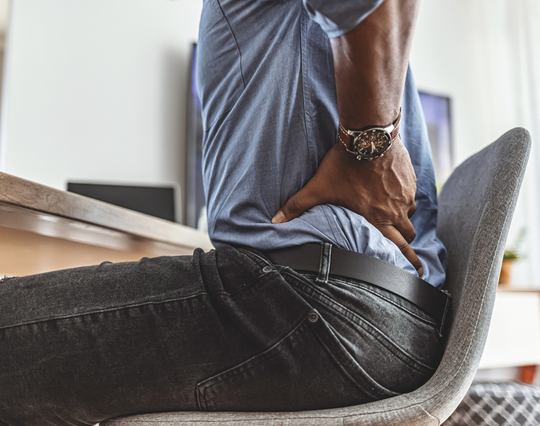A man sitting in a chair and holding his lower back