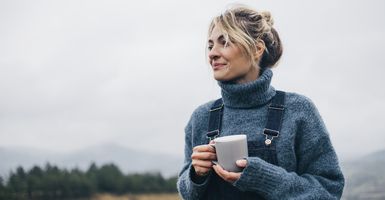 woman in sweater holding a mug in a field