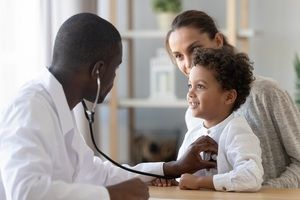 smiling young boy in mom's lap getting checked by doctor