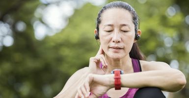 a woman taking her pulse while looking at her fitness watch after exercising outdoors. 