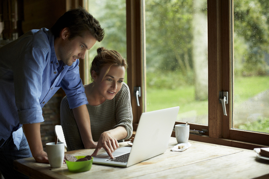 Young couple sitting at the table looking at their laptop