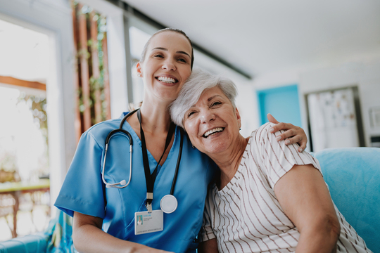 Smiling nurse hugging senior woman at home