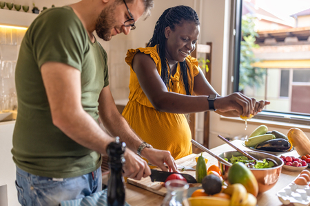 a man and a pregnant woman are cooking healthy food in their kitchen