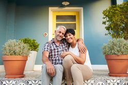 Couple sits on brightly painted patterned tile porch between terra cotta planters