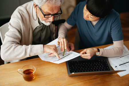 Senior man reviewing health documents with at-home nurse