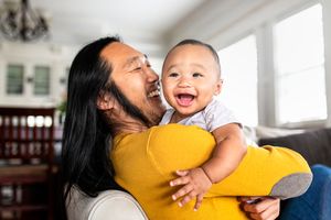 smiling dad in bright sweater holding happy infant