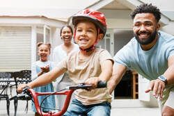 dad helping little boy learn to ride his bike with family cheering