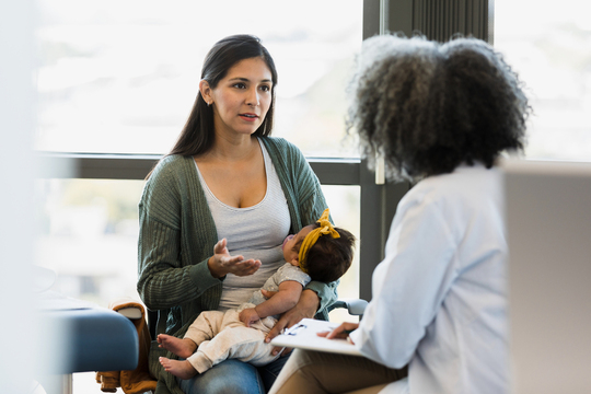 a woman holding an infant while having a discussion with a doctor