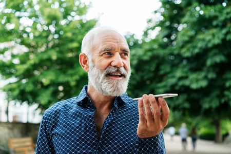Bald man using speakerphone setting on smartphone at outdoor park