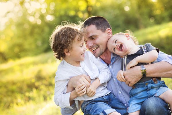 father playing with toddler and older brother on lap outside