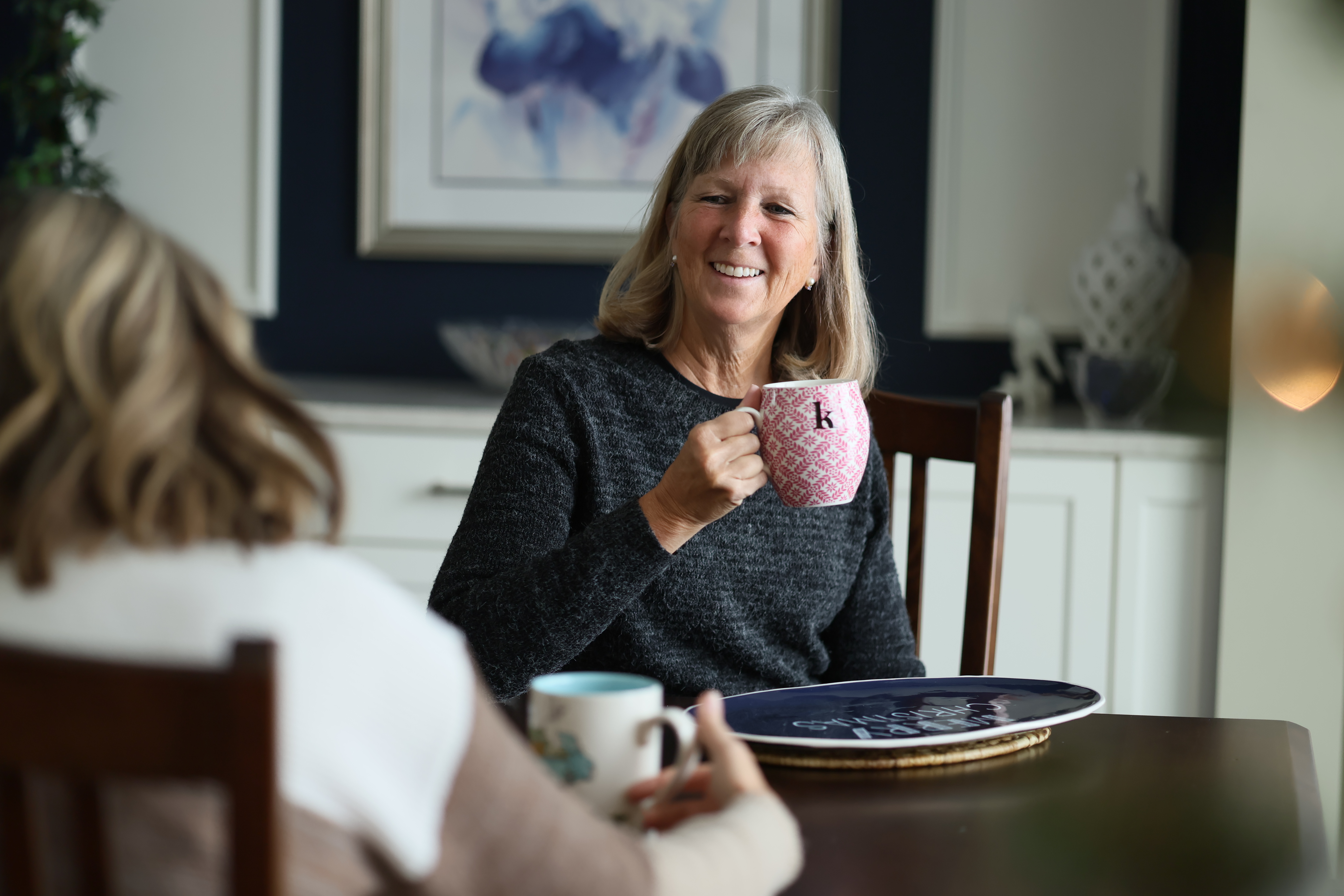 Karen drinking a mug of coffee with a friend at her kitchen table