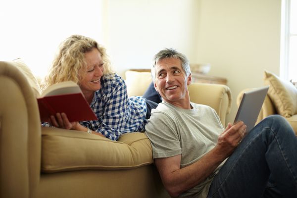 smiling middle age couple in living room reading and looking at tablet