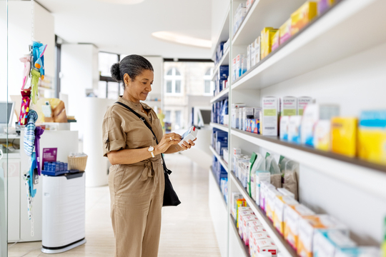 a woman standing in a pharmacy aisle reading the box of a medicine