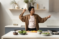 a young woman dances in her modern kitchen behind a counter of health food