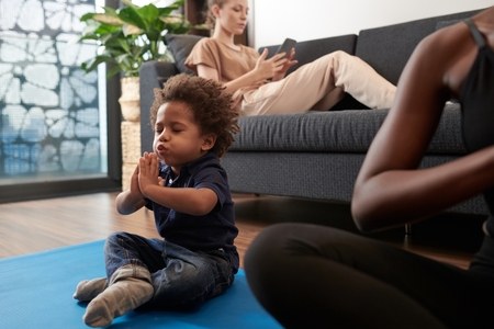 little boy sits on yoga mat in meditation stance, taking deep breath with eyes closed