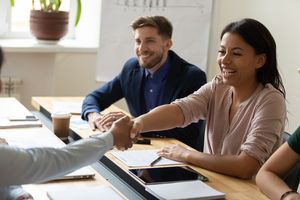 smiling coworkers shaking hands while sitting at conference table in office