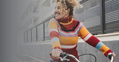 smiling young woman in colorful sweater riding bike