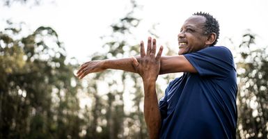 smiling senior man stretching outside in sunshine