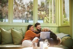 man and woman sitting on couch petting their dog