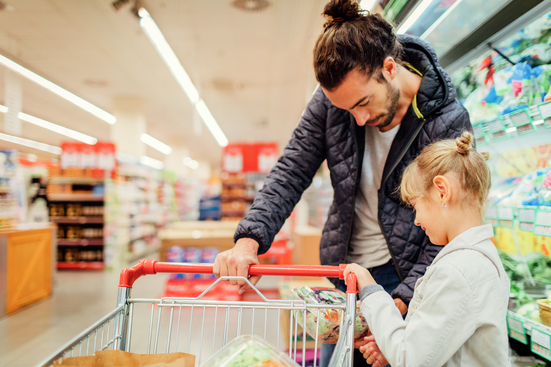 father and daughter pushing shopping cart in grocery store while evaluating food item