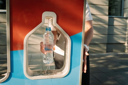 someone filling their plastic water bottle at a community water station outdoors