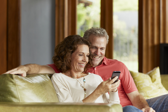 mature couple sitting together on a sofa and smiling at a smartphone