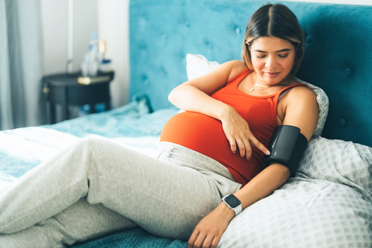 pregnant woman with blood pressure cuff lying in bed