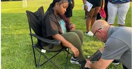 Man fitting sport shoes on kid at a soccer field