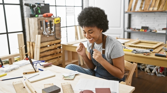 An African-American woman in her last thirties sits at a workbench in her creative workshop