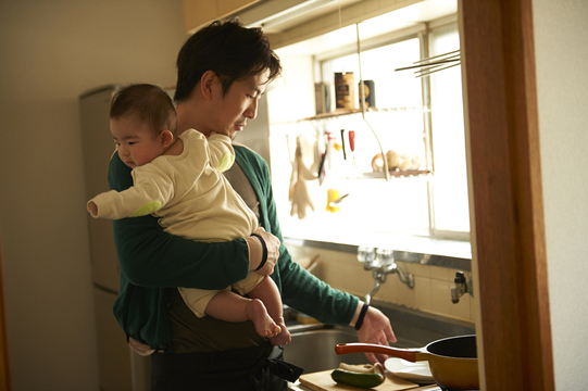 father washing dishes while holding infant 
