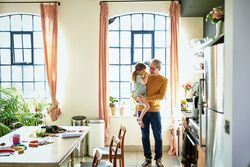 dad holding young daughter in bright kitchen while she drinks from a cup